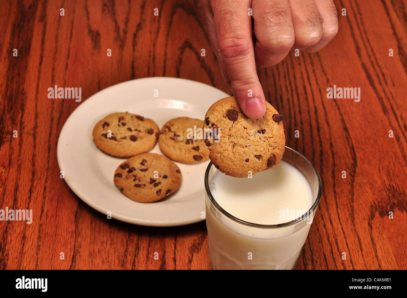 Un cookie è in procinto di essere inzuppati in un bicchiere di latte. Foto Stock