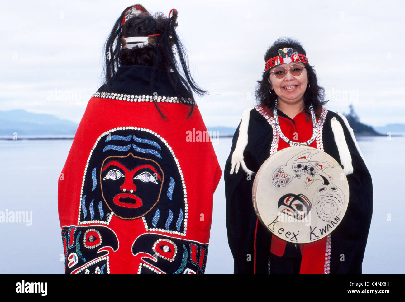 Due Tlingit Native American donne display tradizionale capes progettato con pulsanti e un tamburo della tribù Keex (kwaan) a Kake, Alaska, Stati Uniti d'America. Foto Stock