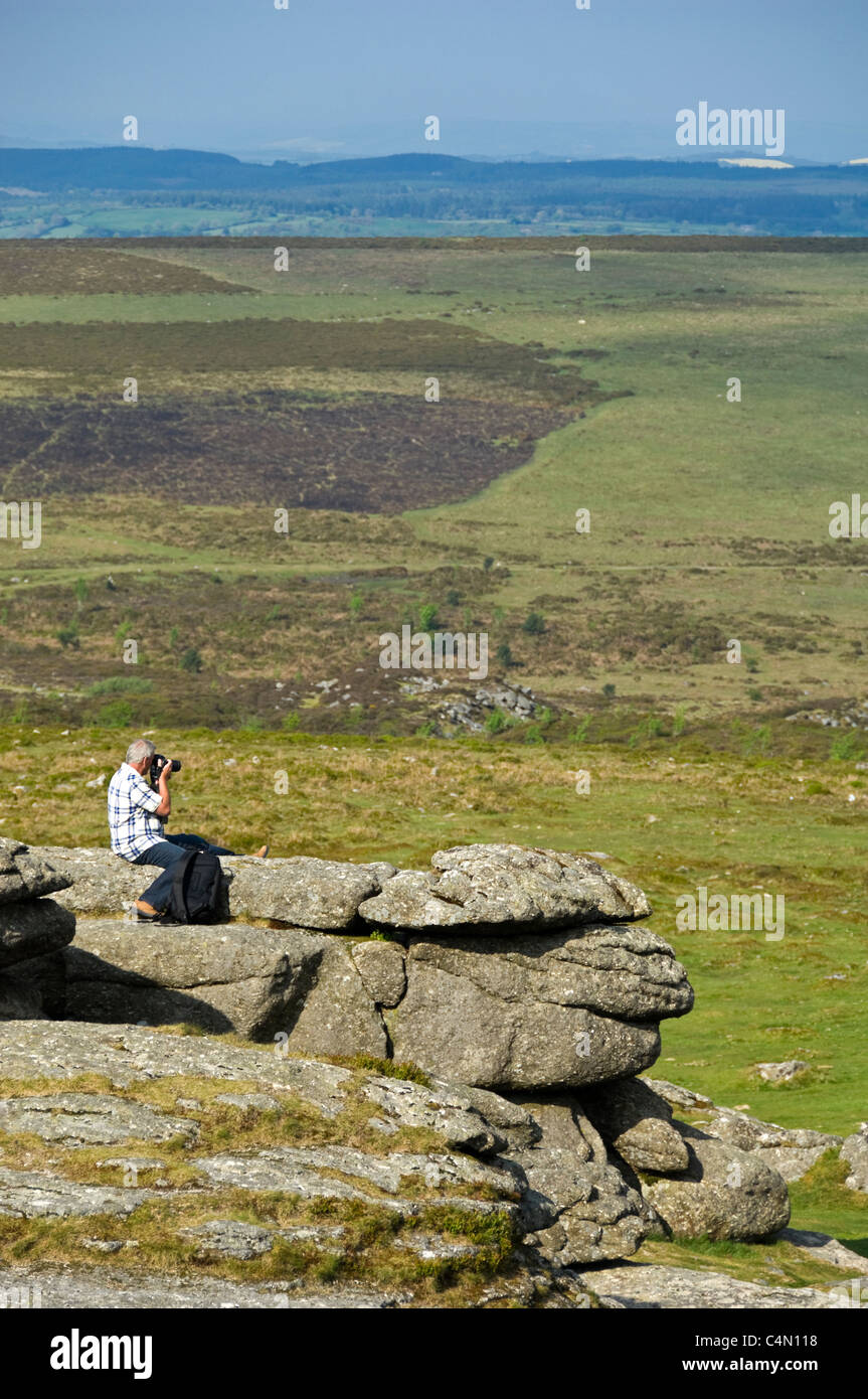 Verticale ampia angolazione di un uomo prendendo fotografie della vista da Haytor o fieno Tor, sul Parco Nazionale di Dartmoor su un giorno d'estate. Foto Stock