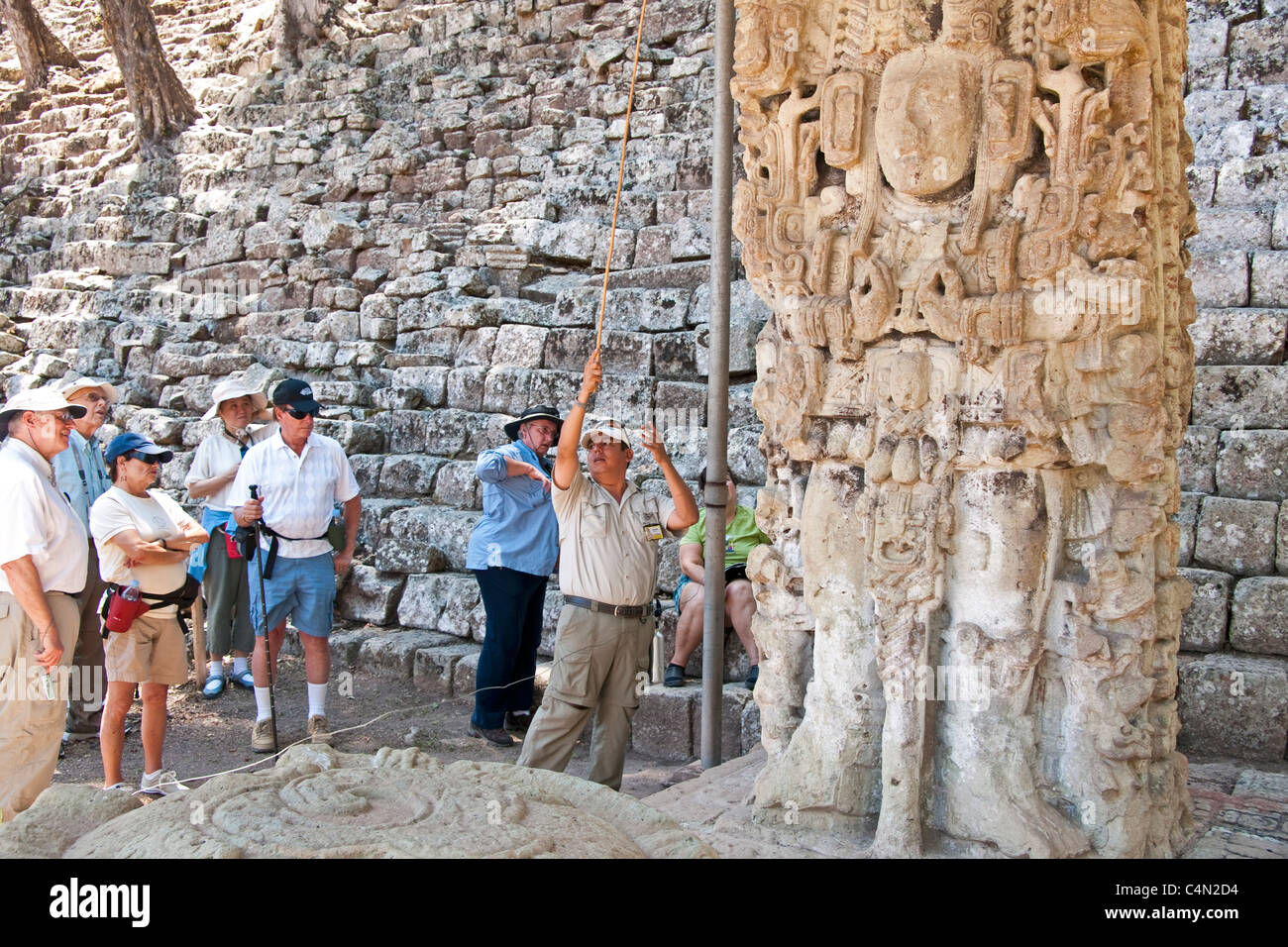 Guida locale con i turisti che descrivono calendario Maya sulla stele in rovina maya di Copan Foto Stock