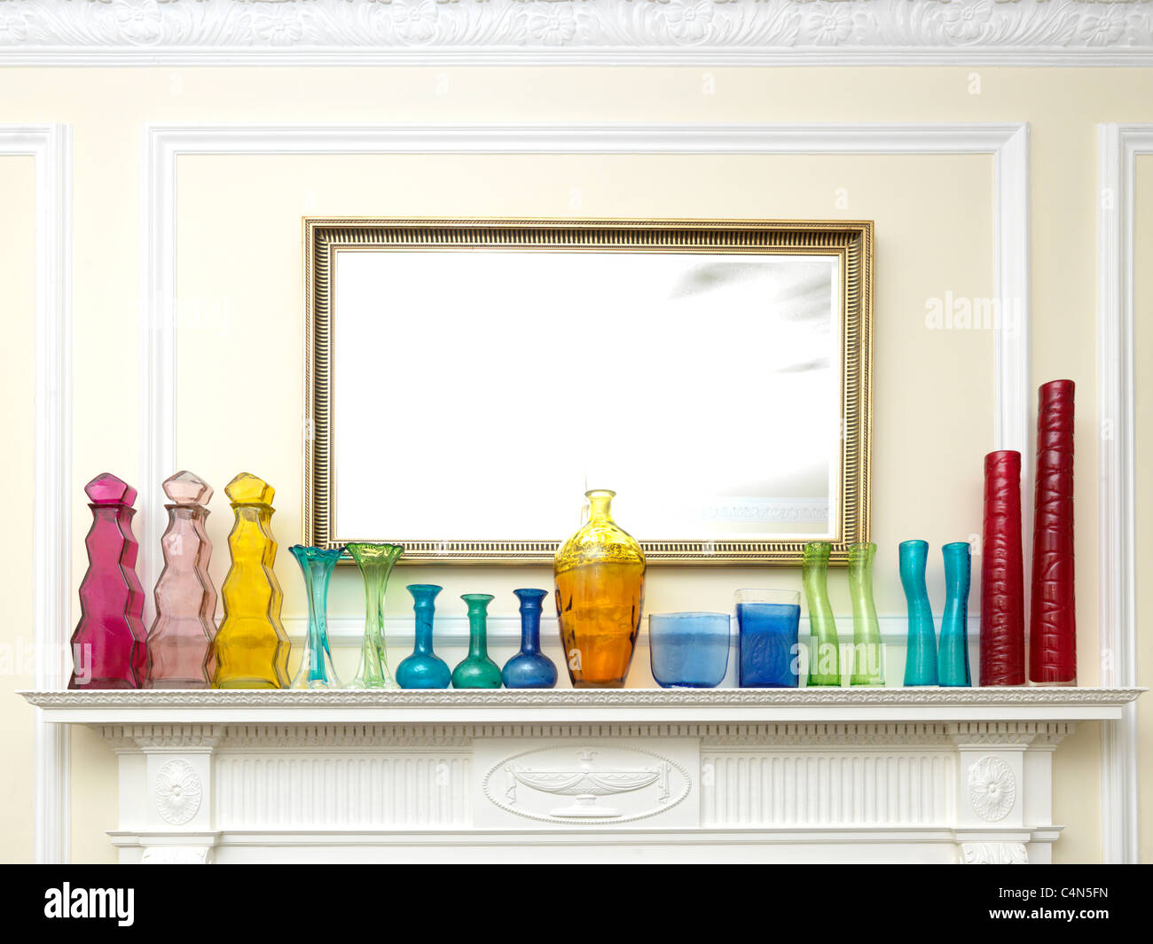 Una raccolta di diversi colori e forme di bottiglie e vasi da vetro riciclato in una fila su un da caminetto da uno specchio Foto Stock