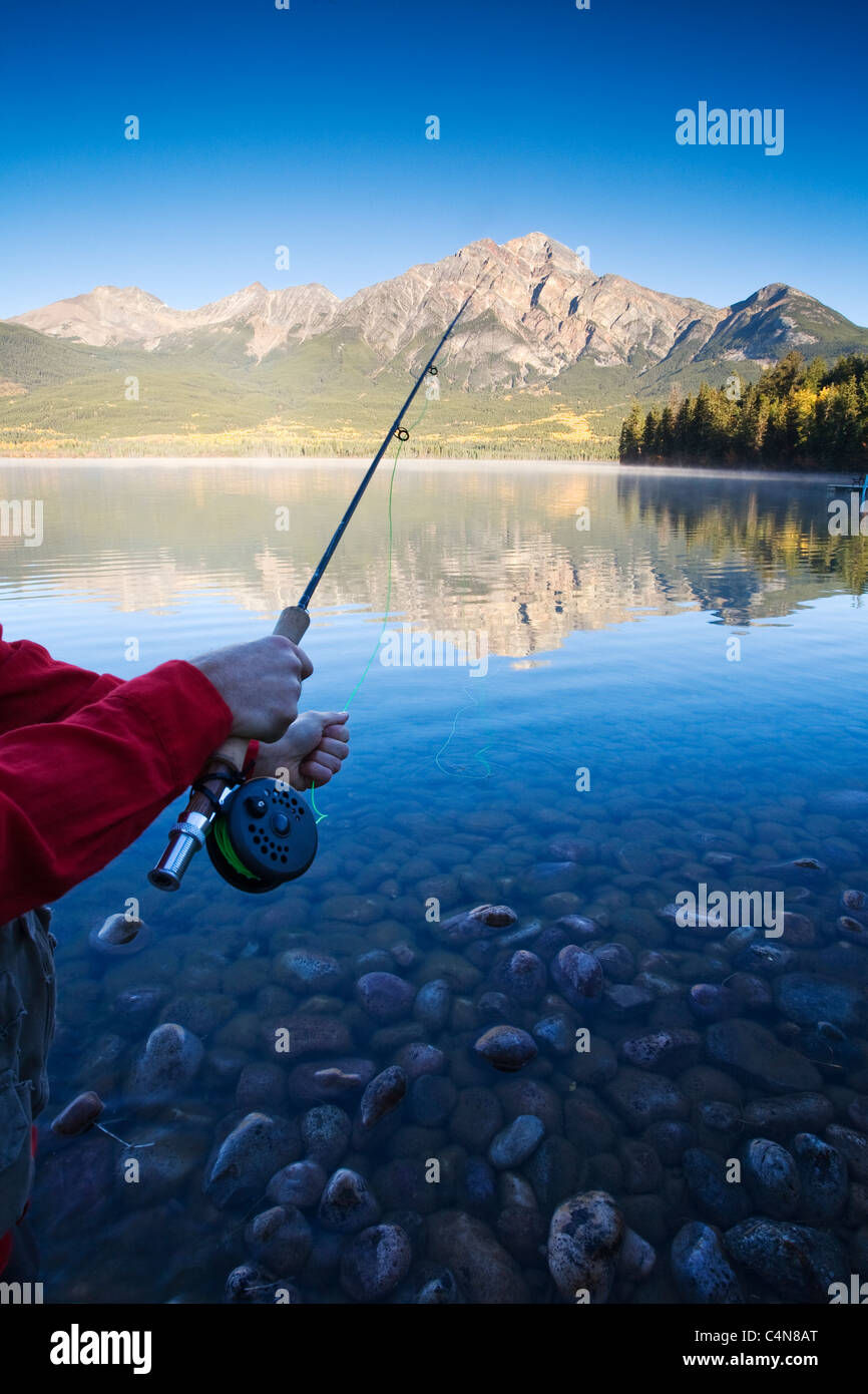 Vicino la mano sulla canna da pesca all'alba, Lago Piramide, il Parco Nazionale di Jasper, Alberta, Canada. Foto Stock
