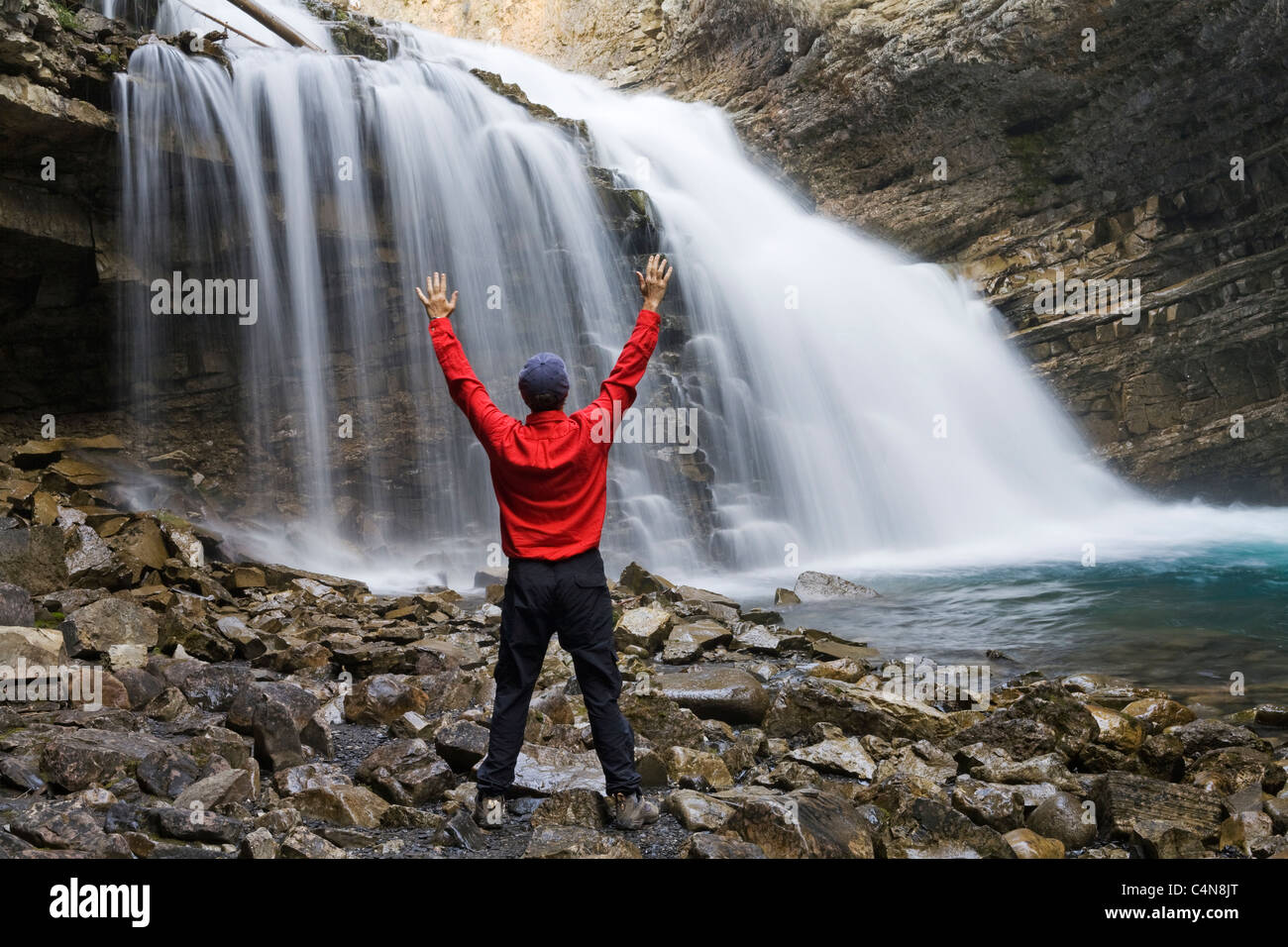 Escursionista di fronte a cascata con bracci sollevati, Johnson Canyon, il Parco Nazionale di Banff, Alberta, Canada. Foto Stock