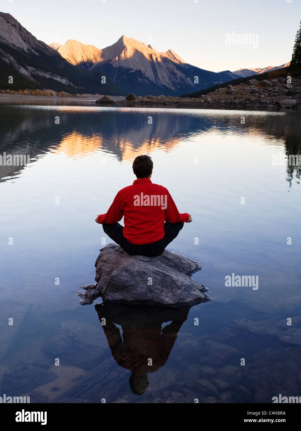 La mezza età uomo meditando su roccia sulla medicina Lake, il Parco Nazionale di Jasper, Alberta, Canada. Foto Stock