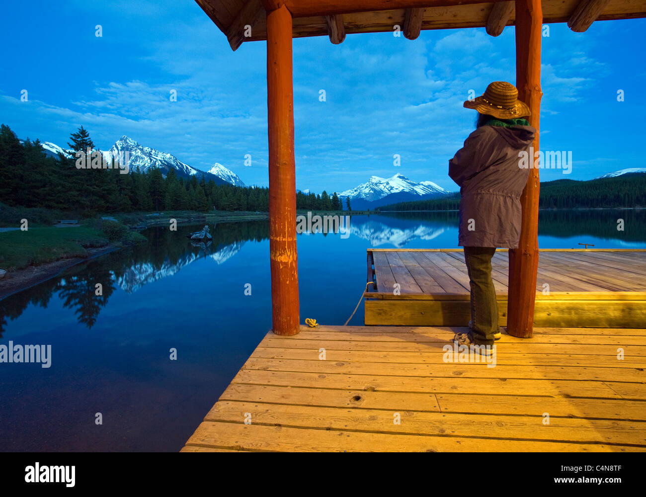 Donna che guarda le montagne su dock del Lago Maligne boathouse al tramonto, il Parco Nazionale di Jasper, Alberta, Canada. Foto Stock