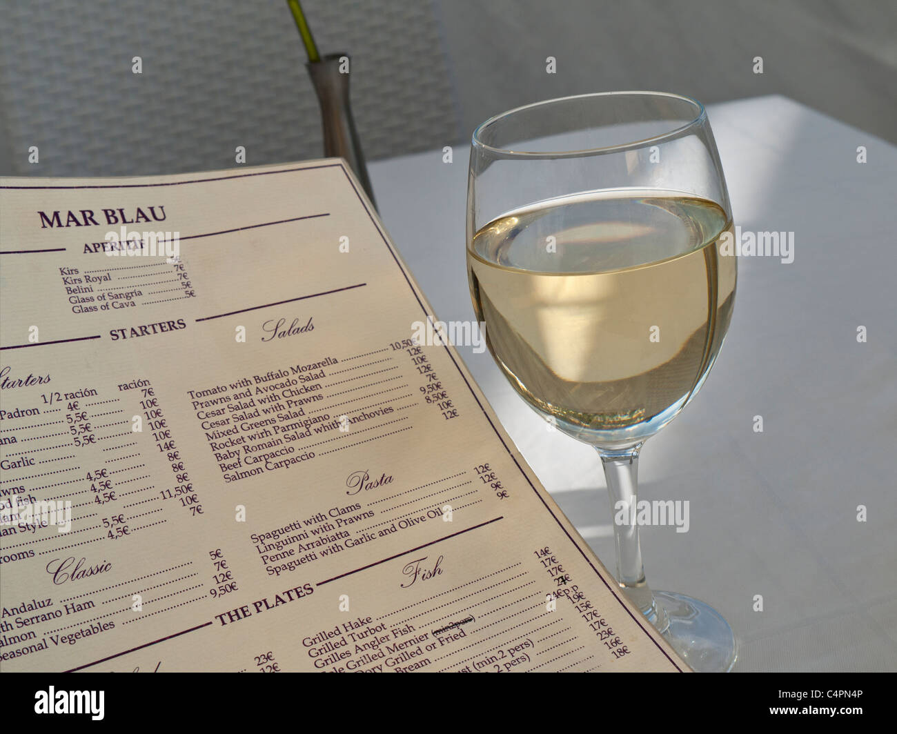 MENU BICCHIERE DI VINO SPAGNOLO TAVOLO ALL'APERTO SUN SHAFT bicchiere di vino bianco di maiorchino e menu del ristorante al tavolo Palma Mallorca Spagna Foto Stock