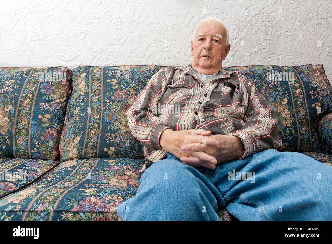 Un pensionato anziano Senior uomo seduto su un divano nel suo soggiorno a casa. Foto Stock