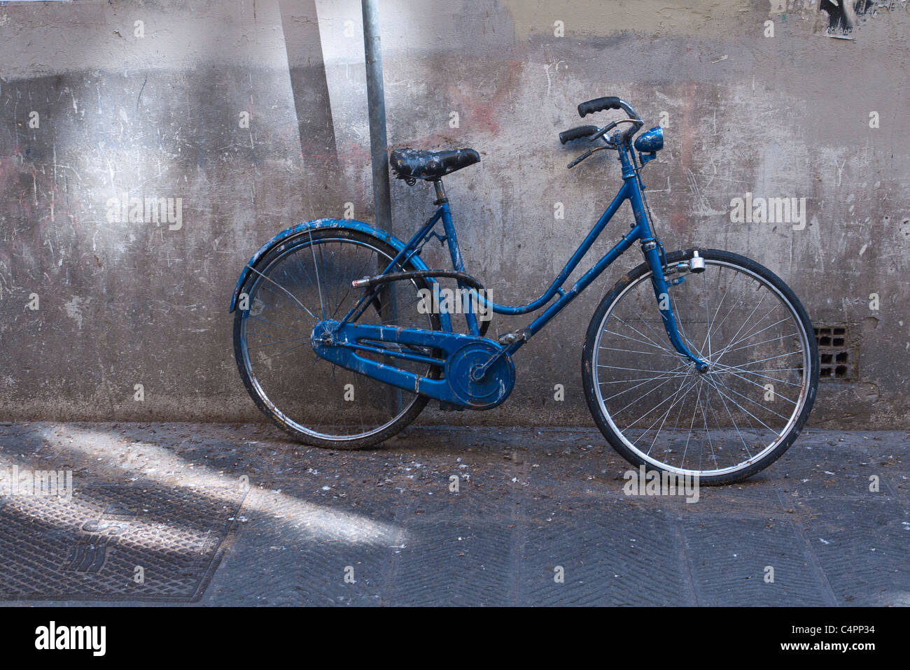 Una donna blu bici si appoggia contro una parete in ombra in Firenze, Italia. Foto Stock