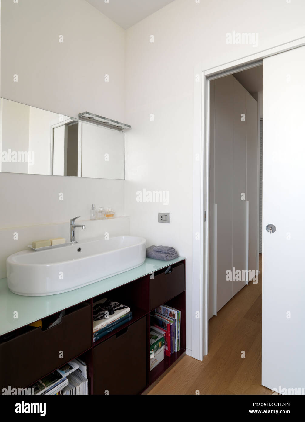 Bagno moderno con pavimento in legno e lavabo bianco, porta scorrevole. Foto Stock