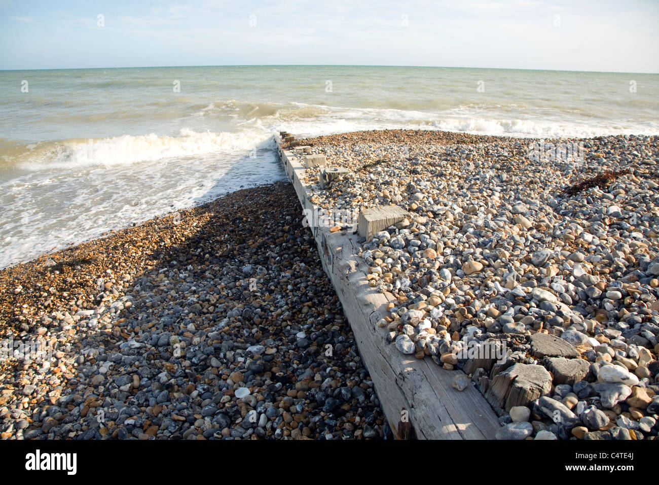 Deriva di Longshore illustrato da sedimenti su entrambi i lati del groyne in legno sulla spiaggia ghiaiosa Foto Stock