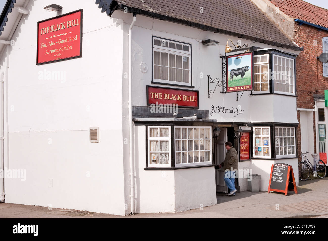 L'esterno del Black Bull (tradizionale pub o locanda storica bianca in inglese) insegne e uomo che entra - Boroughbridge, Yorkshire, Inghilterra, Regno Unito. Foto Stock