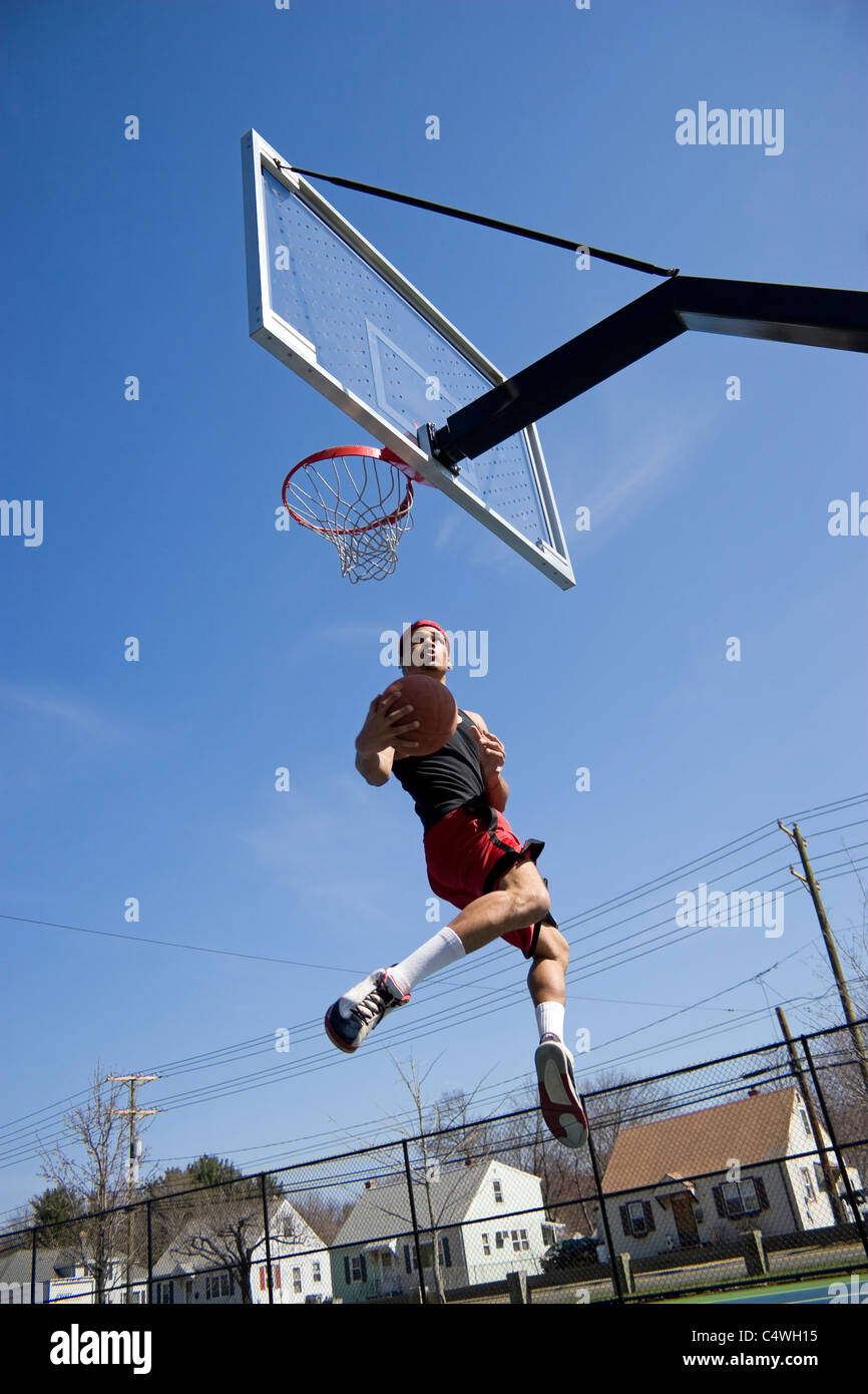 Un giovane atleta guida per il basketball hoop per un lay up o Slam Dunk. Foto Stock