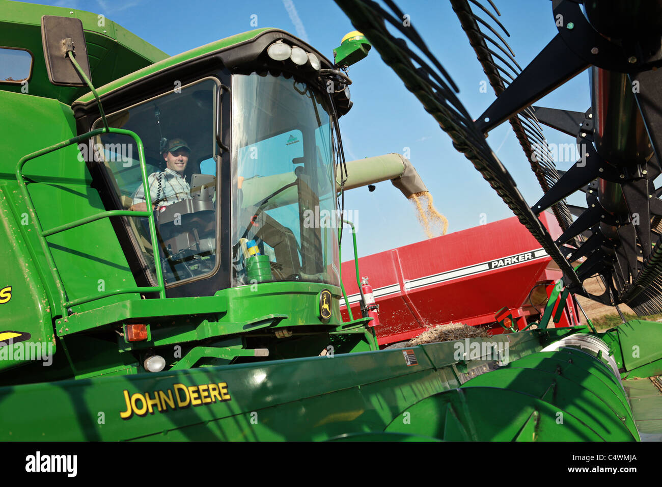 L'agricoltore lo scarico di fagioli di soia a raccolto da una mietitrebbia John Deere in un carro del grano in Iowa. Foto Stock