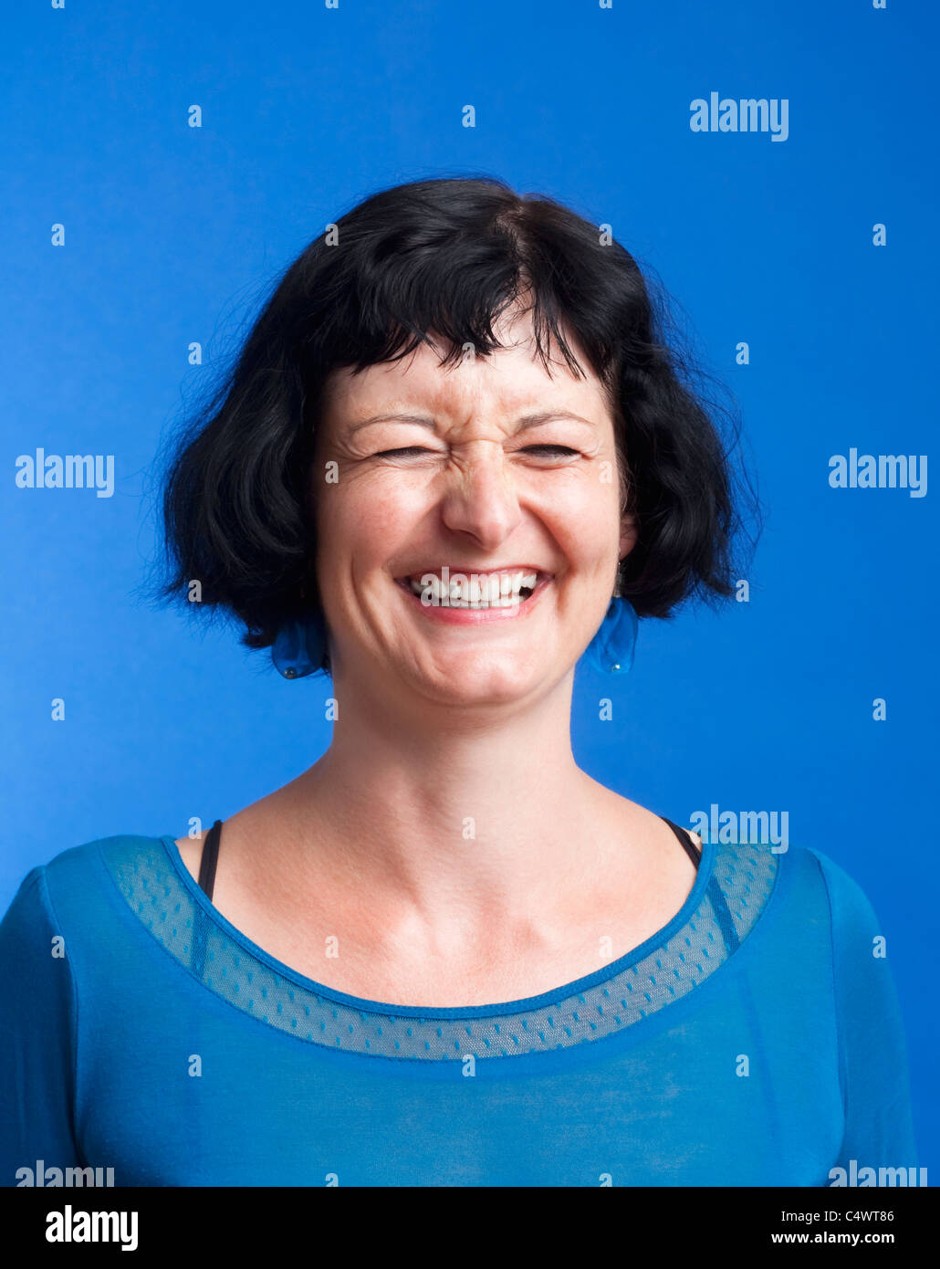Ritratto di donna di mezza età con i capelli scuri di ridere - isolato su blu Foto Stock