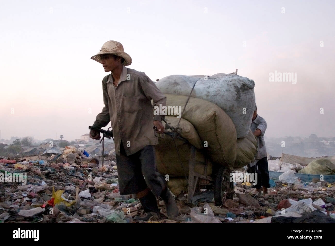 I lavoratori sono il trasporto di sacchi di immondizia in un tossico e inquinata dump cestino in Cambogia. Foto Stock