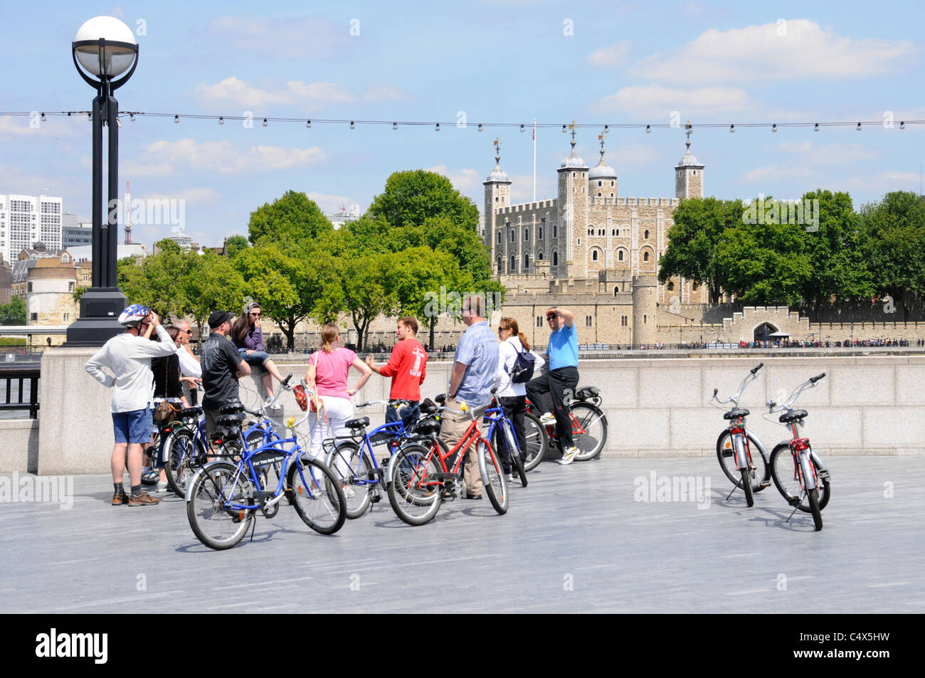 Gruppo di turisti che utilizzano biciclette a noleggio durante la gita turistica con accompagnatore ascoltando la guida turistica (in rosso) di fronte alla Torre di Londra accanto al Tamigi Inghilterra UK Foto Stock