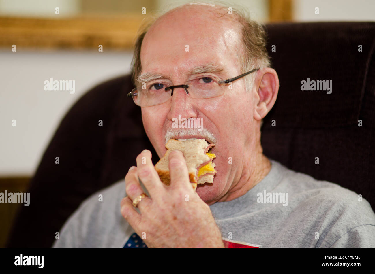 Un anziano uomo mangia un panino mentre è seduto in una poltrona reclinabile. Stati Uniti d'America. Foto Stock