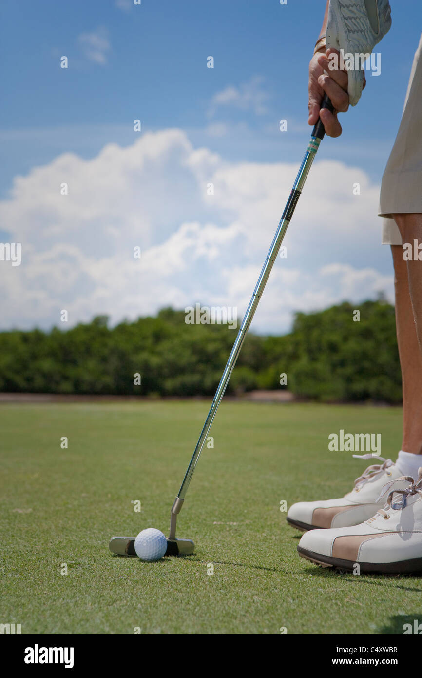 Focus su il golfista allineando il suo colpo, leggermente sfocati sullo sfondo di un prato e si avvicinano nuvole all'orizzonte Foto Stock