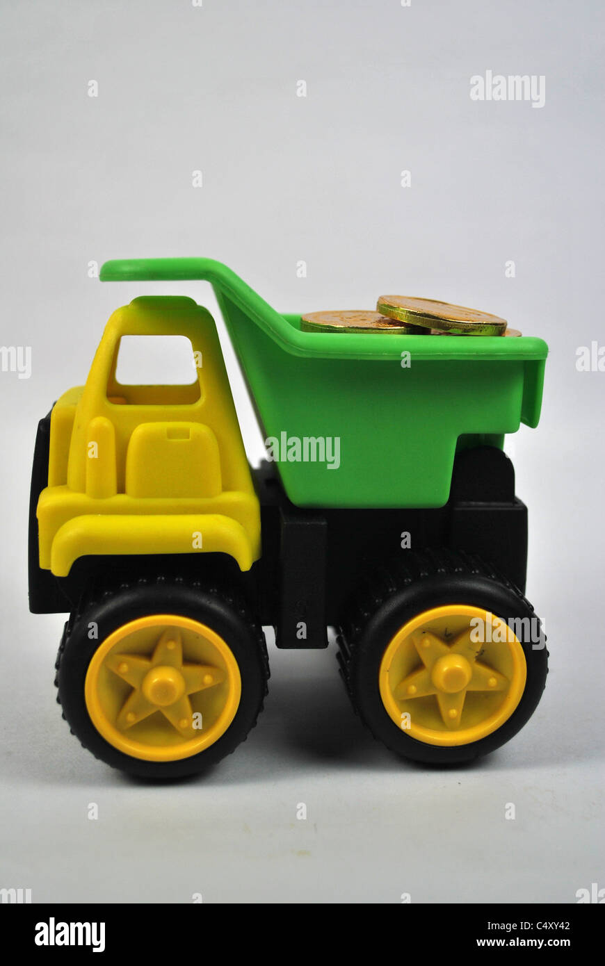 Toy giocoso autocarro autocarro auto mobile wealth denaro moneta in oro silo tagliare cut-out retro bianco terreno isolato giallo verde nero Foto Stock