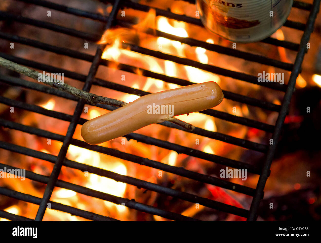 Un hotdog su un bastone di essere cotta su un fuoco Foto Stock