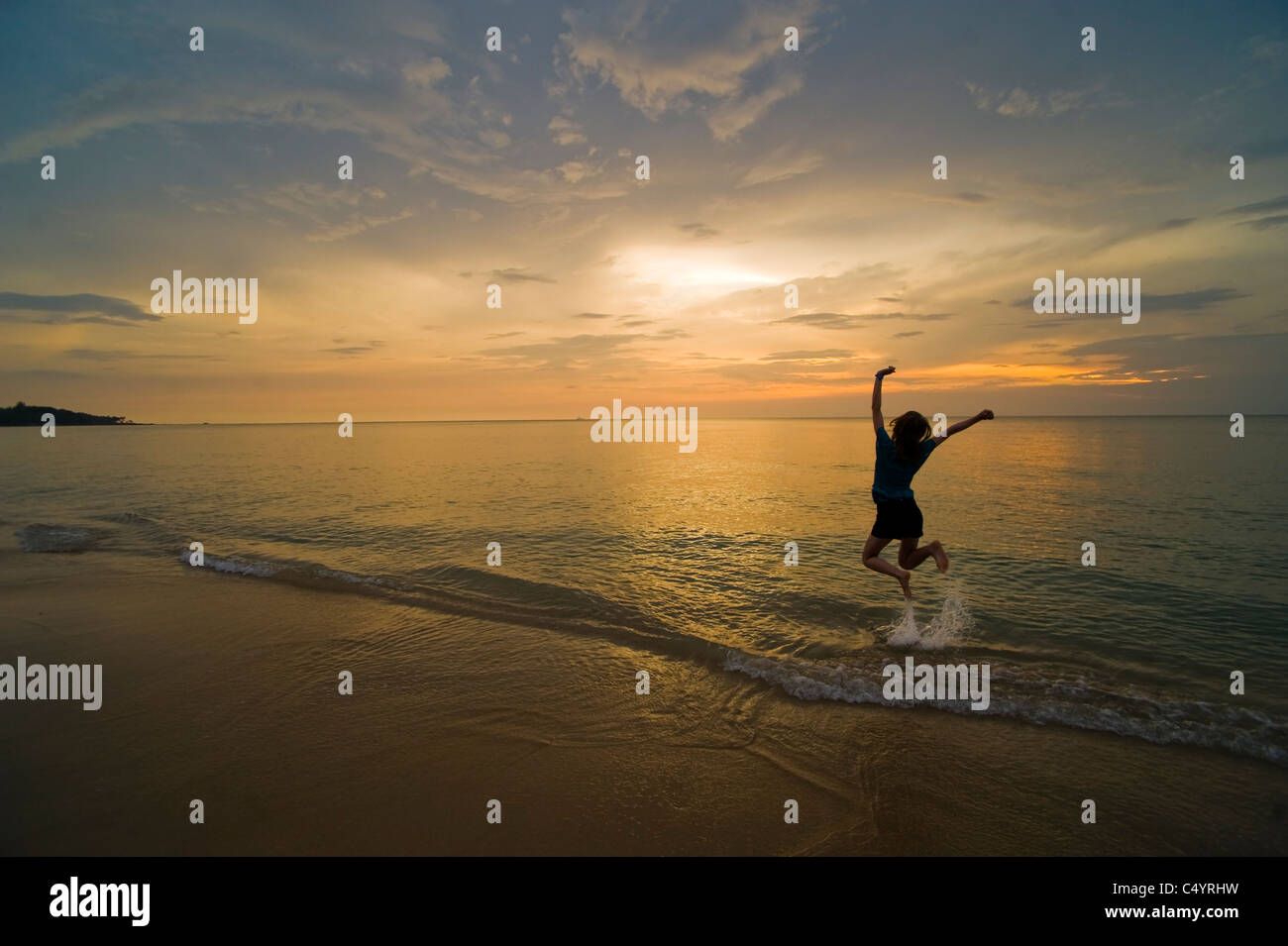 Una giovane donna salti di gioia e di celebrare sulla spiaggia al tramonto. Preso in Phra Ae Beach, Koh Lanta, sud della Thailandia Foto Stock