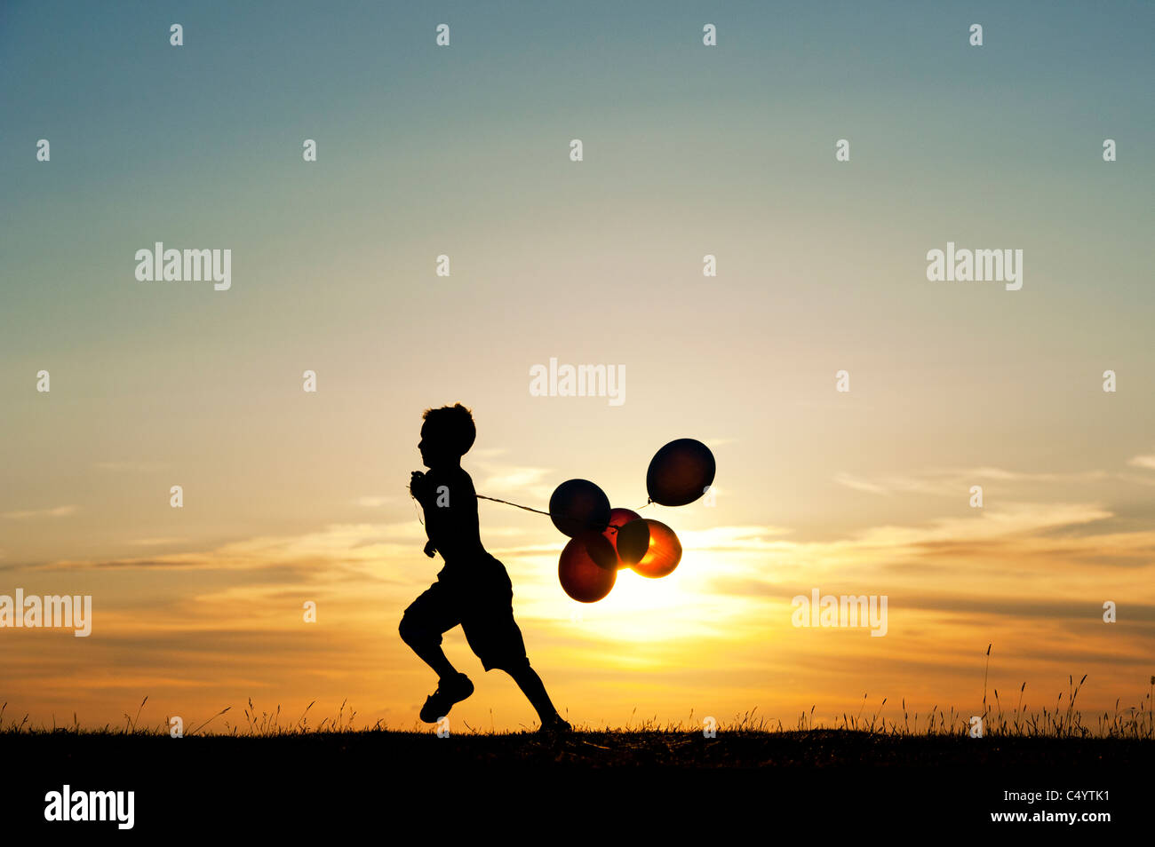 Silhouette di un giovane ragazzo in esecuzione con palloncini al tramonto Foto Stock