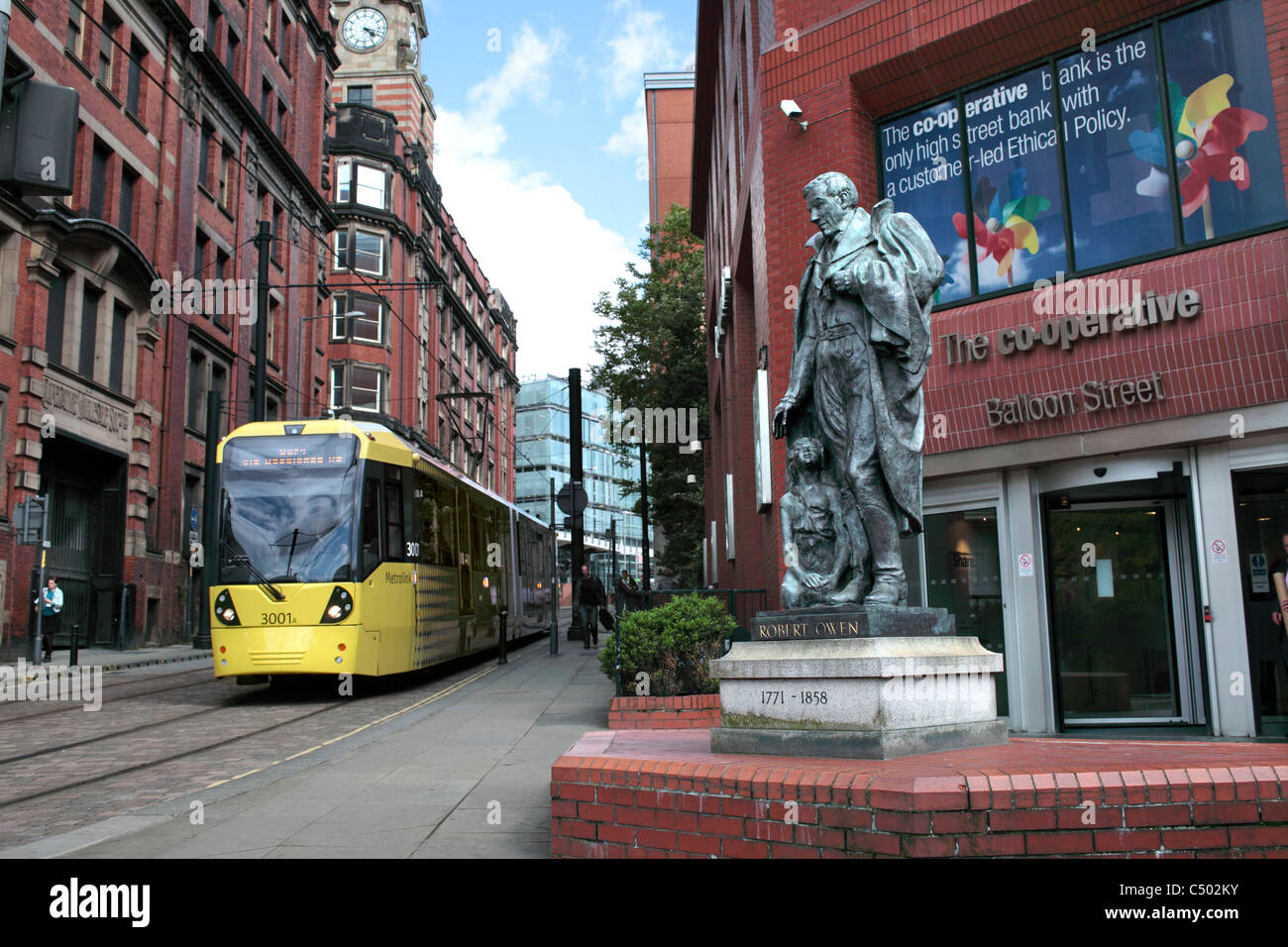 Una fermata del tram che passa una statua di Robert Owen al di fuori della Co-op Bank sul palloncino Street, Manchester. Foto Stock