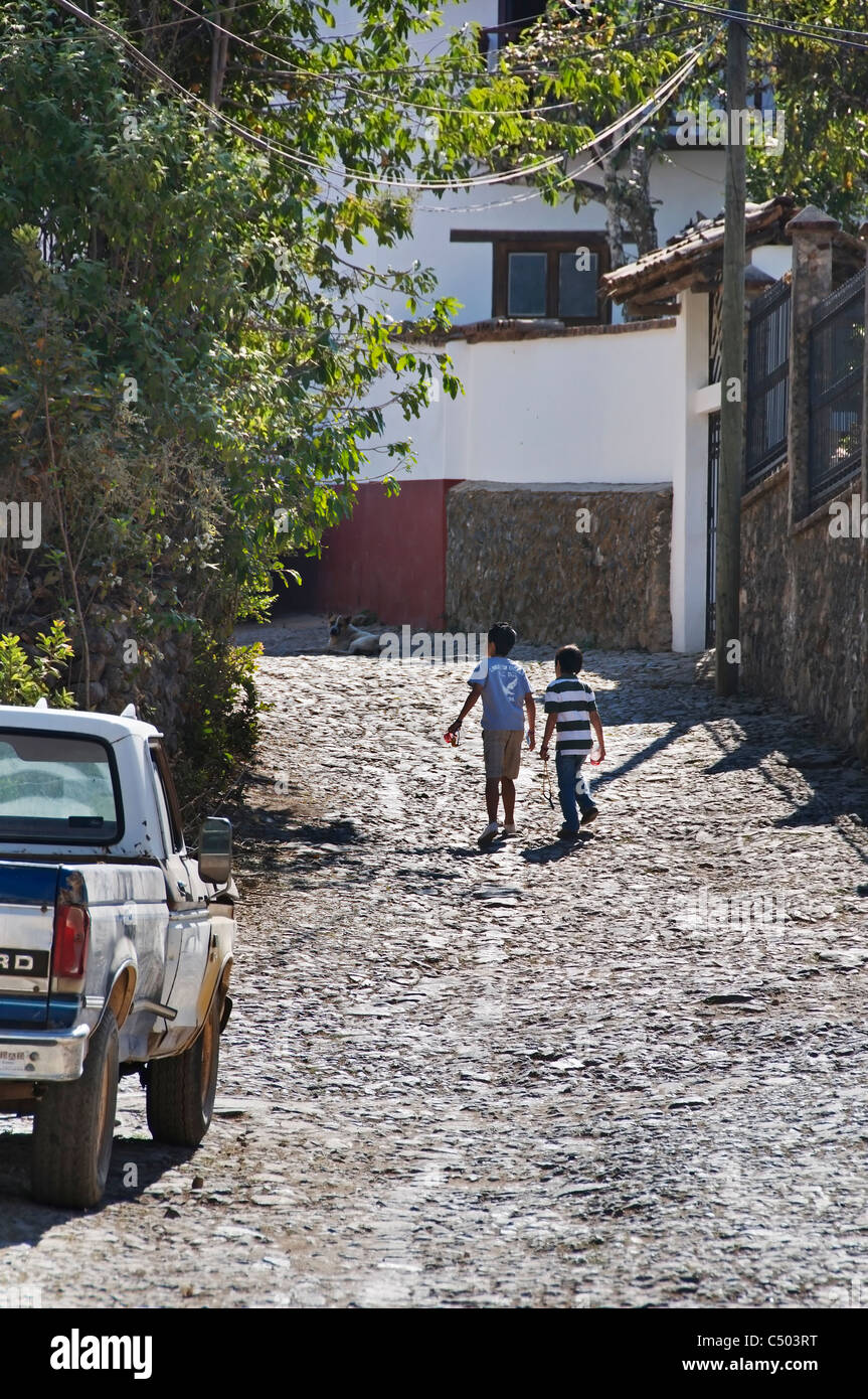 Vista posteriore di due ragazzi a camminare su una stretta strada di ciottoli a San Sebastian del Oeste, Jalisco, Messico. Foto Stock