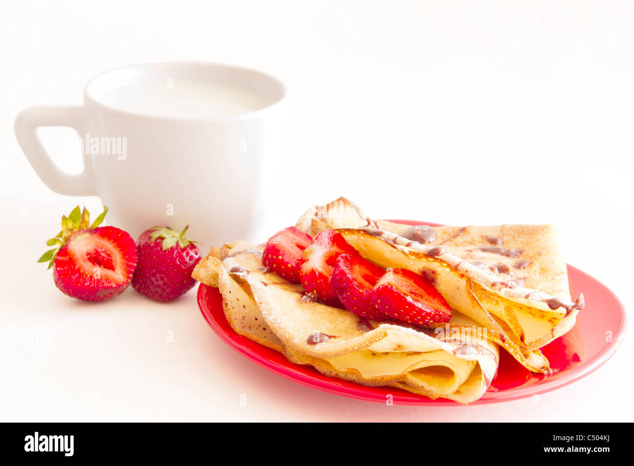 Frittelle dolci con fragola e tazza di latte su sfondo bianco Foto Stock