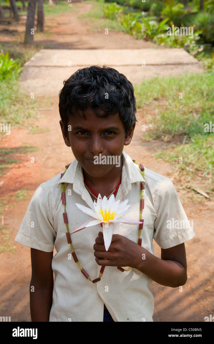 Un ragazzo tenendo un fiore di loto nelle lagune del Kerala a Quilon, India. Foto Stock