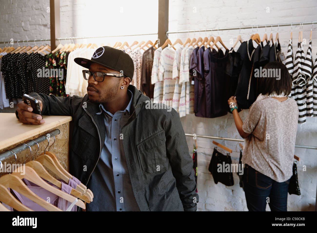 African American uomo di messaggistica di testo sul telefono cellulare in negozio di abbigliamento Foto Stock