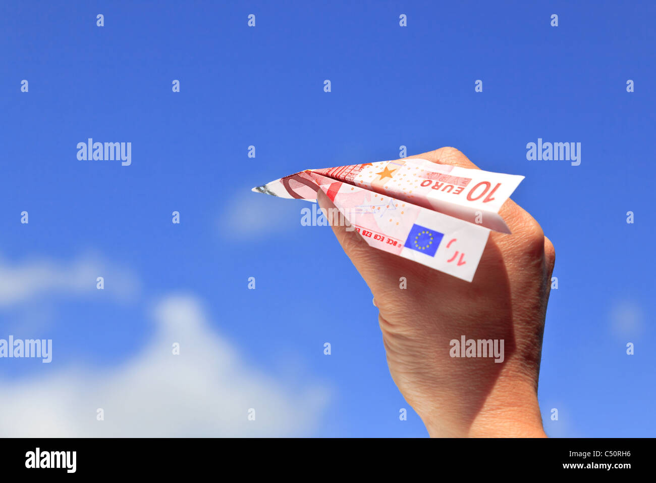 Foto di una mano womans circa il lancio di una decina di banconote in euro aeroplano di carta in cielo in una giornata di sole. Foto Stock