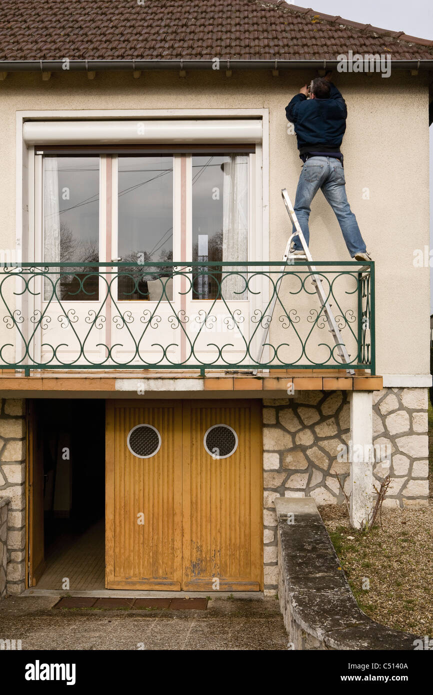 Uomo in piedi sulla scala, di effettuare interventi di manutenzione all'esterno della casa Foto Stock