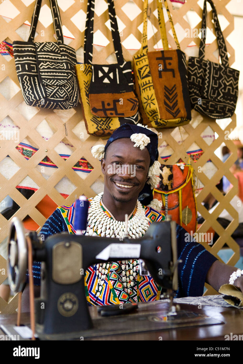 Un sorridente sarto keniota in abiti tradizionali seduti dietro una macchina da cucire Foto Stock
