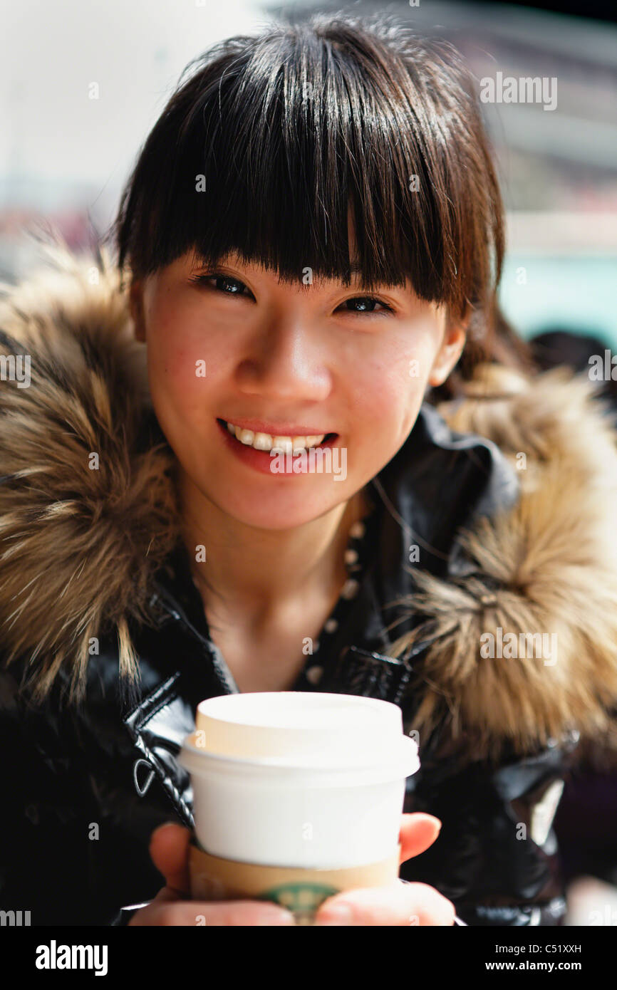 Giovane donna asiatica tenendo una tazza di caffè in un cafe' all'aperto e sorridente, Citta' di Xian, Cina Foto Stock