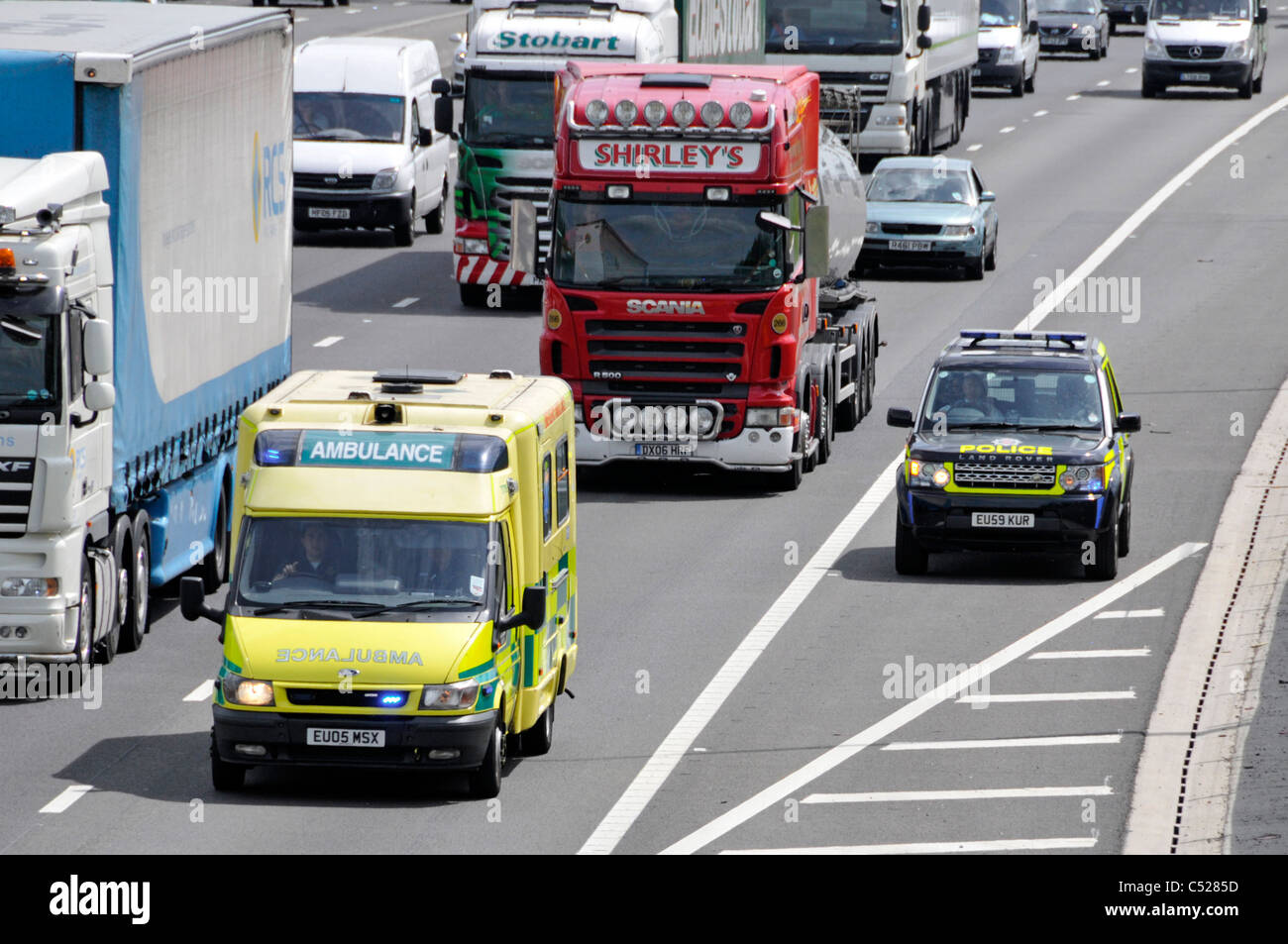 Servizi di emergenza luci su ambulanza & driver di polizia autostrada pesante traffico sul modo di incidente utilizzando una corsia & hard spallamento M25 Inghilterra Essex REGNO UNITO Foto Stock