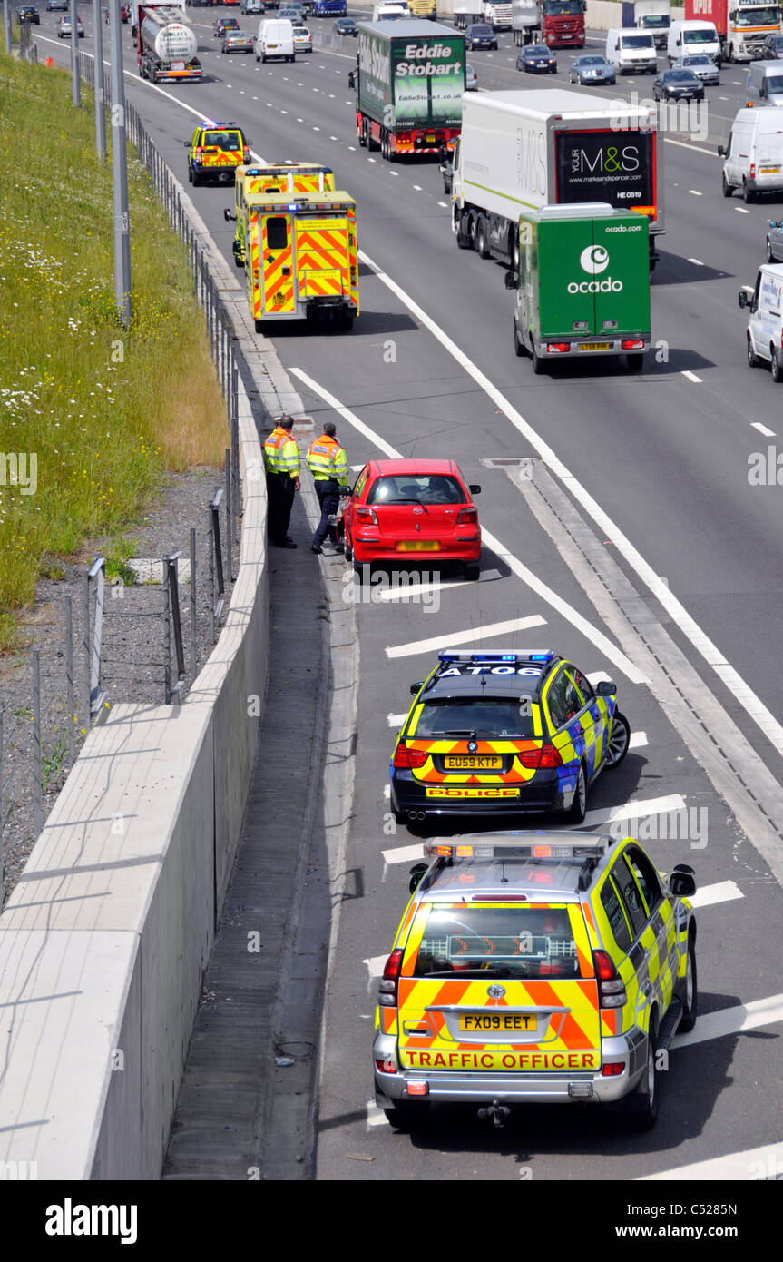 Vista dall'alto guardando verso il basso sulla rossa auto autostrada dopo il crash si trasferì a disco spalla parcheggiato servizi di emergenza veicoli M25 Autostrada Essex England Regno Unito Foto Stock
