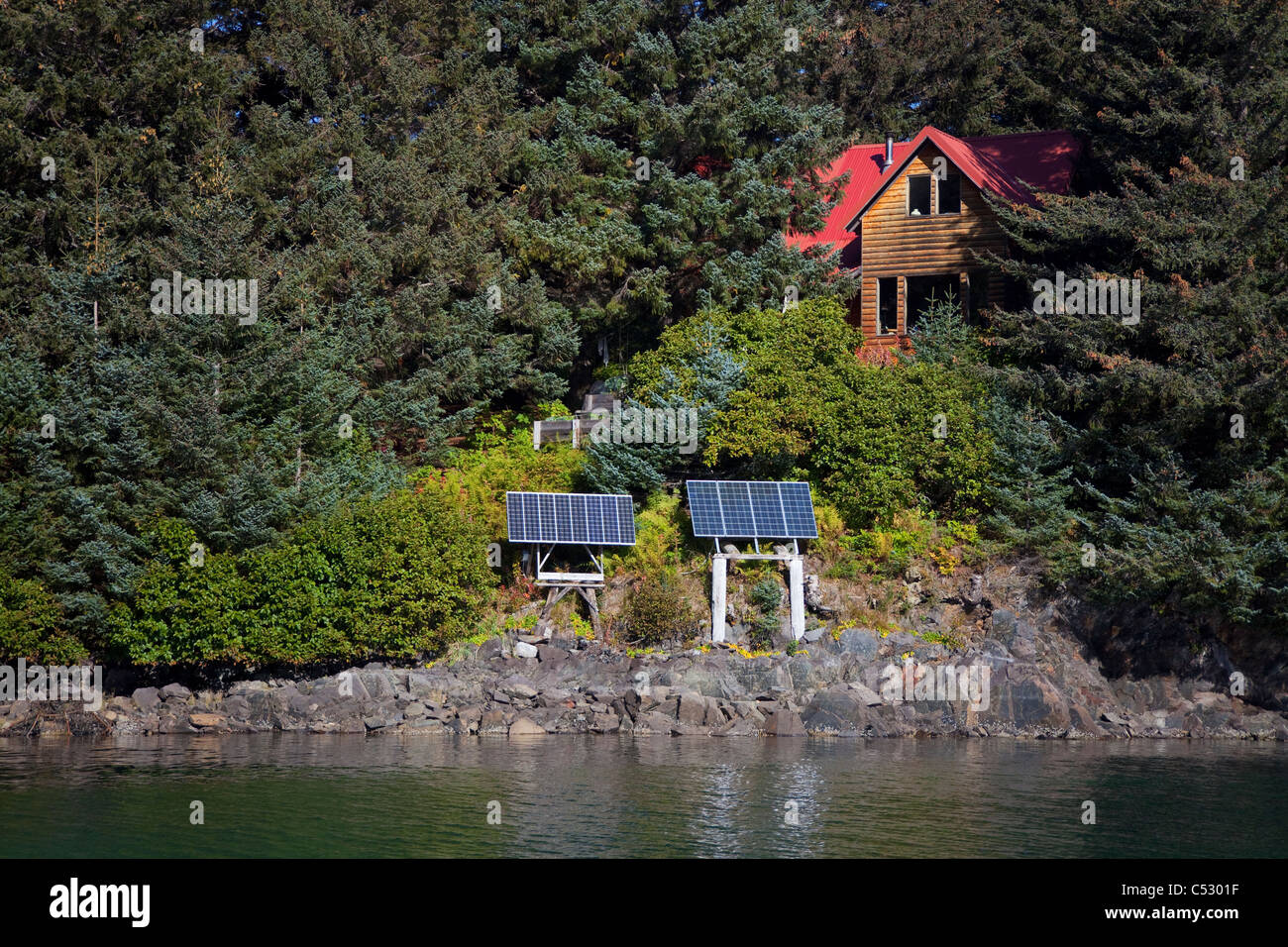 Vista panoramica di un log home alimentato da pannelli solari in Anton Larsen Bay, isola di Kodiak, Southwest Alaska, estate Foto Stock