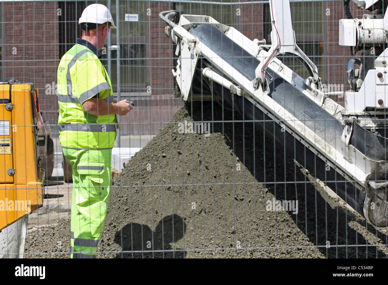 Un operaio guardando aggregato che viene versato in una pila in lavori stradali a Londra in Inghilterra Foto Stock