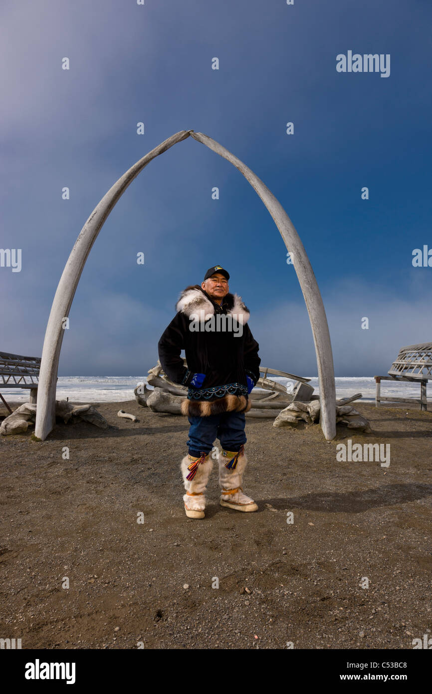 Inupiaq maschio eschimese hunter indossa il suo Eskimo parka , in piedi di fronte a un Bowhead whale osso arch e Umiaqs, Barrow, Alaska Foto Stock