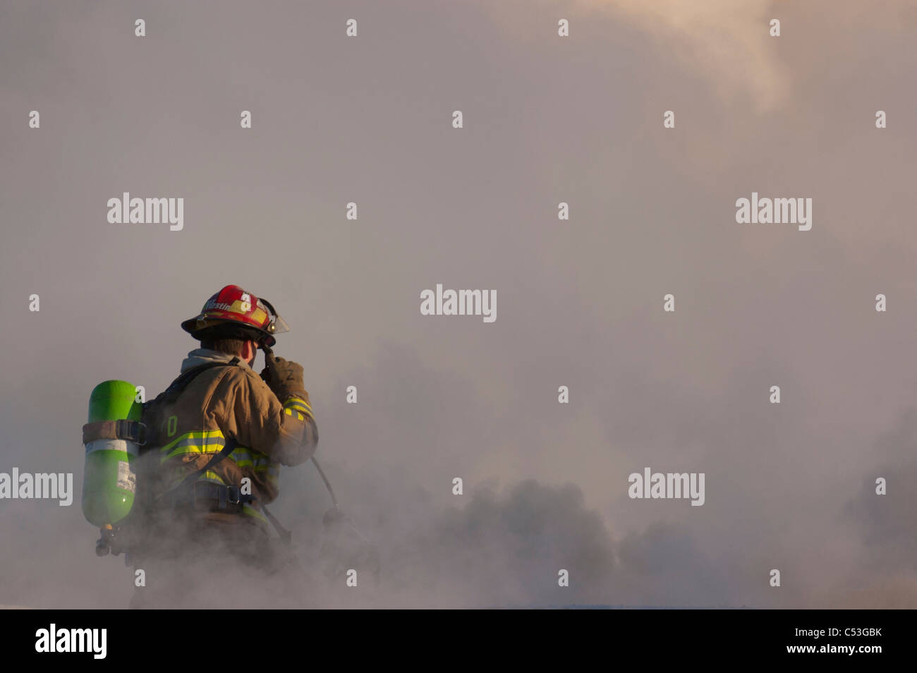 Un ancoraggio dei Vigili del Fuoco pompiere sorge in cima al tetto di un centro di motel mentre si lavora a spegnere la fiamma, Alaska Foto Stock