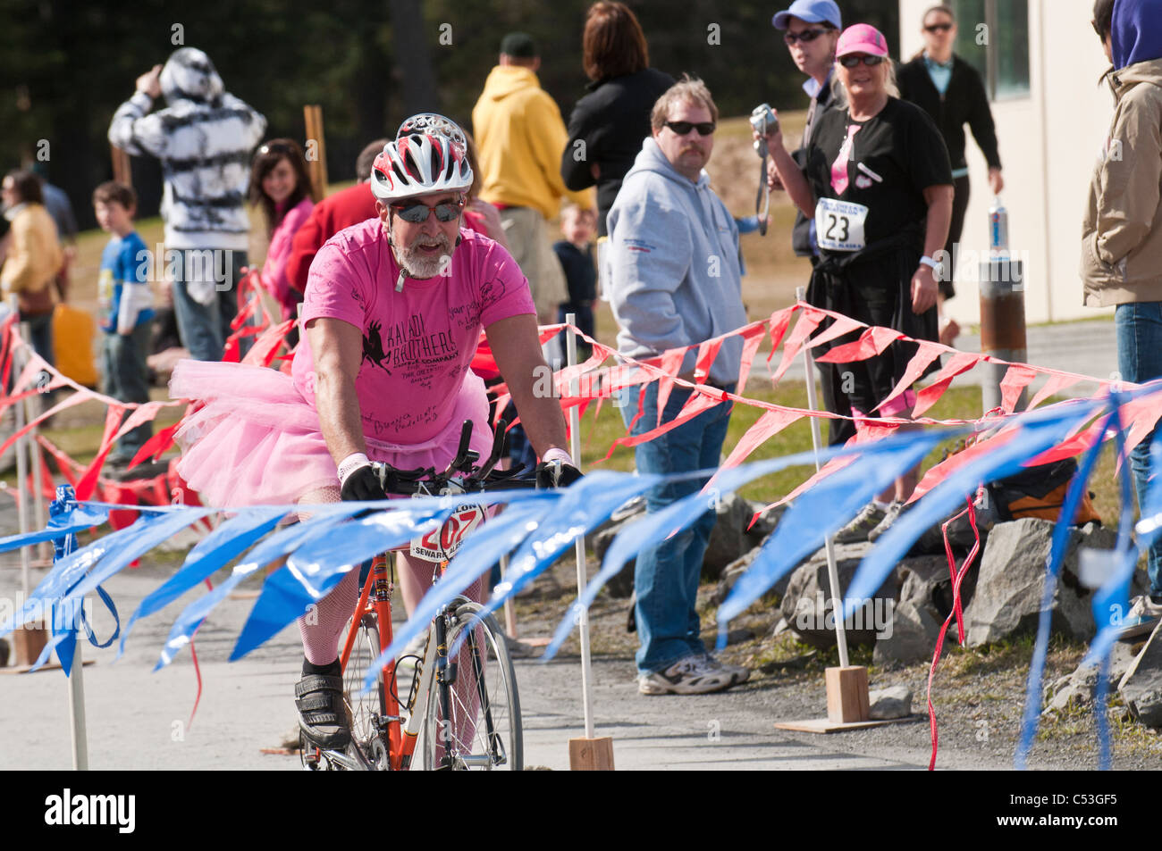 L'uomo vestito di una maglia rosa e costume tutu bici sulla linea del traguardo durante le guance Rosa Triathlon, Seward, Alaska Foto Stock