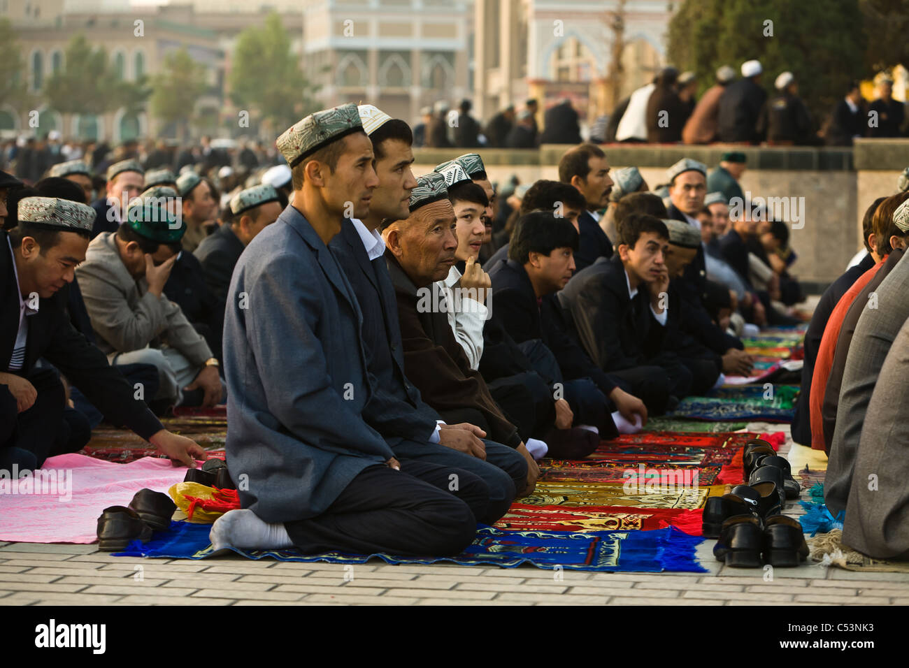 Adoratori di musulmani inginocchiati su tappeti di preghiera al di fuori della Moschea Id kah e alla fine del mese del ramadan. kashgar, provincia dello Xinjiang, Cina Foto Stock