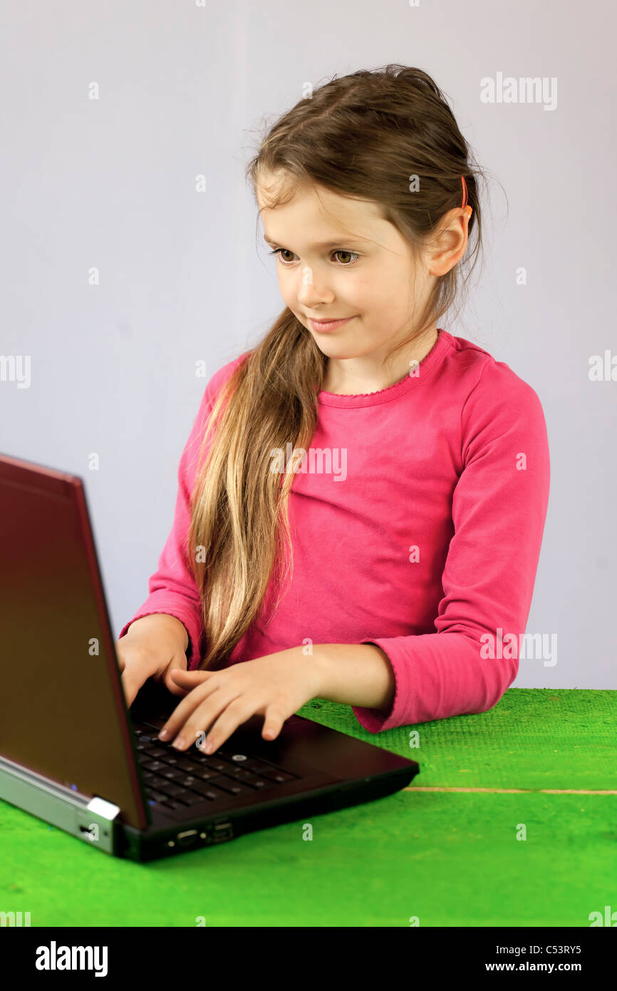 Una bambina di sette anni su un portatile per fare i compiti di scuola Foto Stock