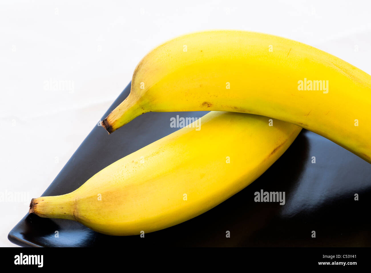 Due delle banane gialle sulla piastra nera. Foto Stock
