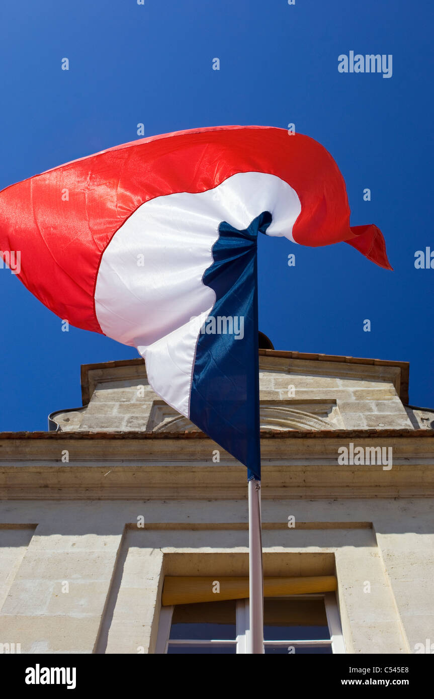 Bandiera francese appeso da un vecchio edificio e volare contro un cielo blu chiaro Foto Stock