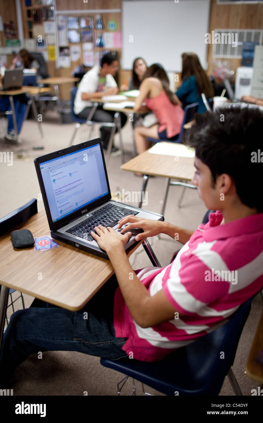 Maschio studente ispanica funziona indipendentemente con computer portatile nella scuola di alta classe come compagni gli studenti lavorano in gruppo Foto Stock