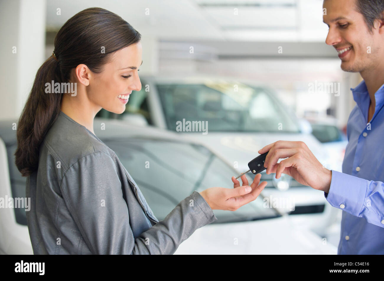 Felice venditore consegna donna chiave auto in showroom Foto Stock