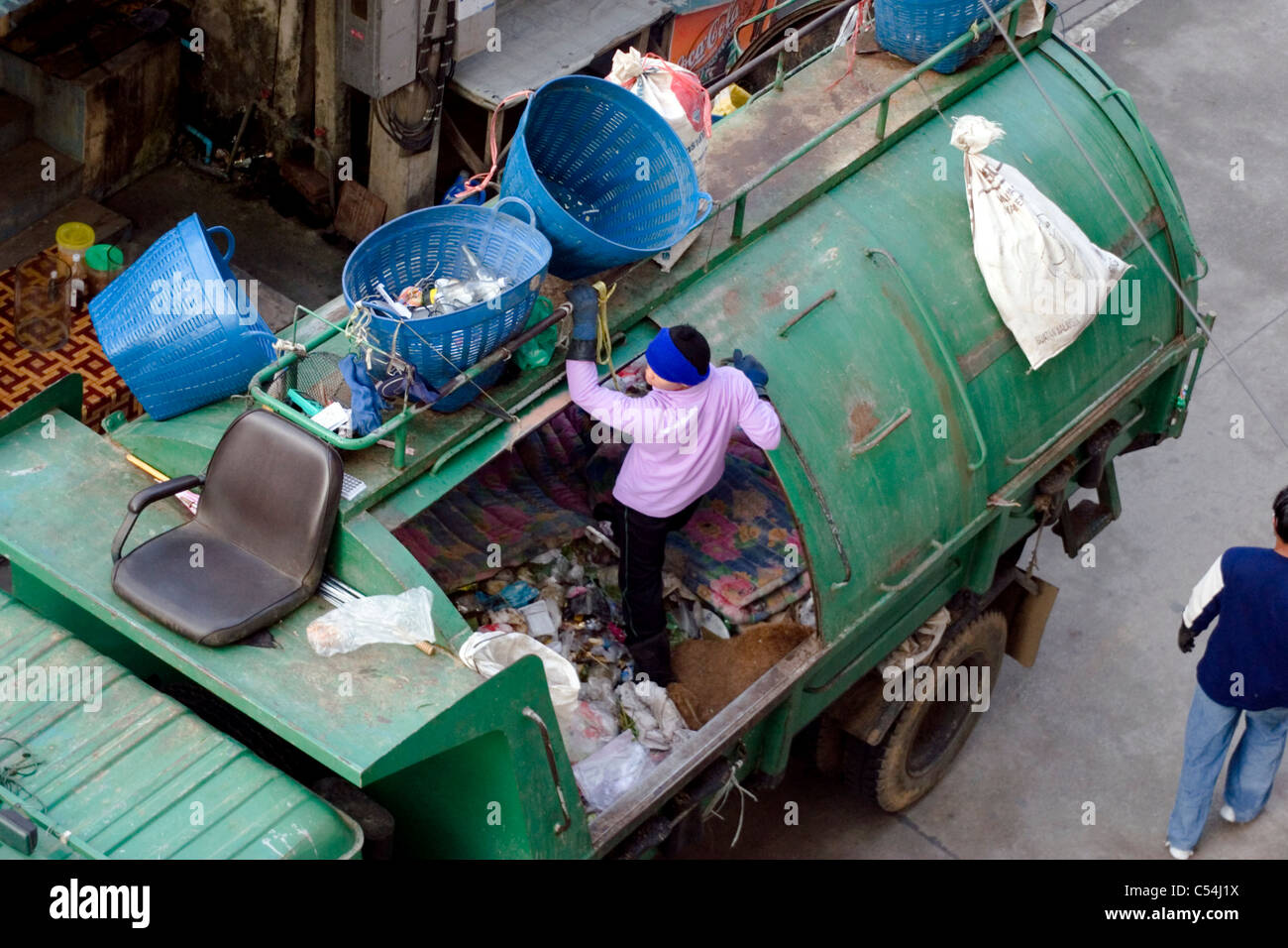Un uomo è in piedi nel cestino durante il caricamento di un camion della spazzatura su una strada di città in Mae Sai, (SAE) Thailandia. Foto Stock