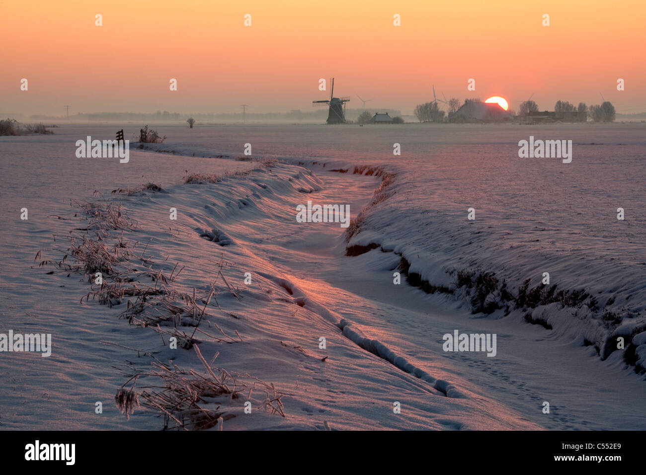 I Paesi Bassi, Lollum, Windmill e congelate in flusso di neve al tramonto. Foto Stock
